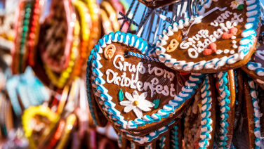 Several colourfully decorated gingerbread hearts hang close together at a market stall. In the foreground, a heart with white icing and a flower can be seen, surrounded by blue and white icing.