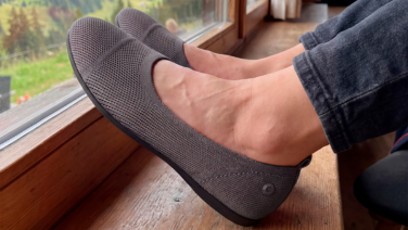 A close-up of a person’s feet, resting on a wooden window sill with their dark trousers rolled up. 