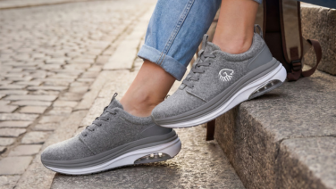 A close-up of a person’s feet in rolled-up jeans, sitting on a stone step. They are wearing grey, mottled merino wool trainers with white soles.