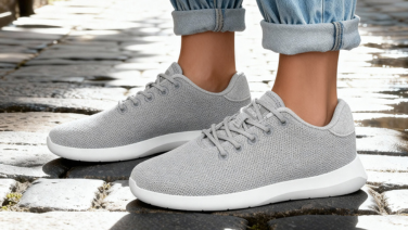 A close-up of a person’s legs in grey Giesswein Wool trainers with white soles. The person is wearing rolled-up jeans and is walking across wet cobblestones.